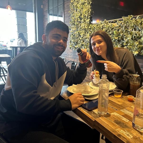 Two happy customers at The Brew Crew NY, one holding a hot sauce bottle, the other pointing at food.