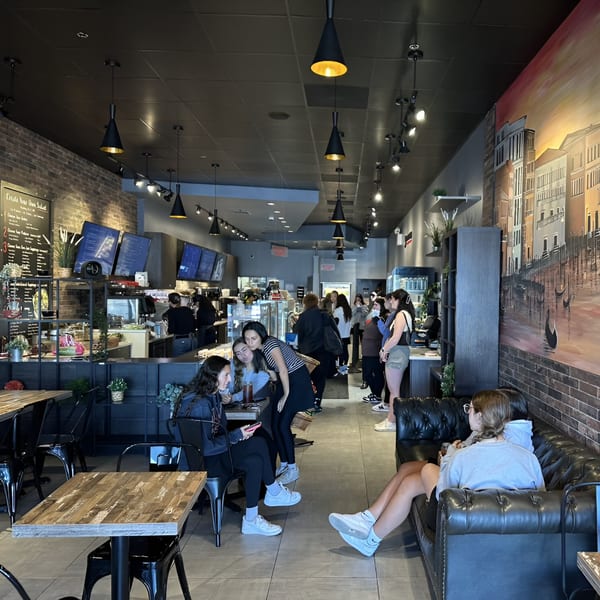 The Brew Crew NY coffee shop interior with customers, tables, and a large mural of Venice.